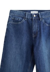 Mörkblå denimjeans med rak bendesign, framfickor och knäppning med en märkt midjebanding.