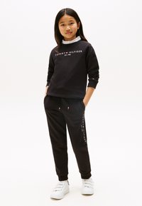Ensemble sweat-shirt noir et joggings avec logo "TOMMY HILFIGER". Tissu en coton, poignets côtelés et taille élastique. Les chaussures sont blanches avec trois bandes.