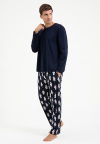 Granatowa bluzka z długim rękawem zestawiona z wzorzystymi spodniami z różowymi i białymi grafikami drzew na ciemnym tle; luźny krój i miękki materiał.