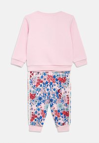 Ροζ φούτερ με μακριά μανίκια συνδυασμένο με φόρμες με λουλουδάτο σχέδιο που περιλαμβάνει κόκκινα, μπλε και ροζ λουλούδια, λευκές πλαϊνές ρίγες και εφαρμοστά μάνικια.