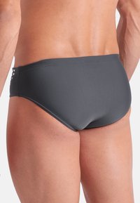 Bañador gris con una textura suave y un diseño de cintura baja. Presenta un patrón de corte decorativo en los lados. Material elástico para mayor comodidad.