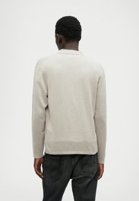 Lys grå langærmet polo sweater med krave og ribbet tekstur, båret med mørke jeans, set fra ryggen.