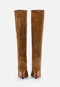 Ein Paar hohe braune Wildlederstiefel mit schlanken Stilettos, von hinten auf einem weißen Hintergrund gezeigt.