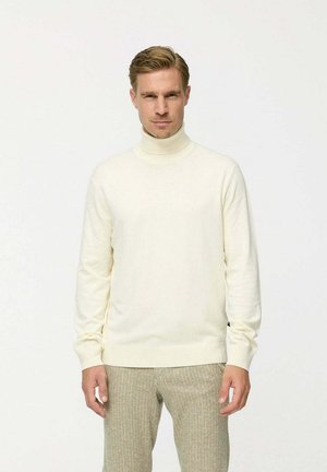 Cremfarbener Rollkragenpullover aus weichem Strickmaterial, mit langen Ärmeln und tailliertem Schnitt. Kombiniert mit hellen, strukturierten Hosen.