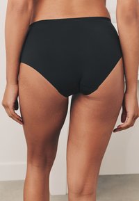 Czarne bikini z wysokim stanem o gładkiej fakturze, z umiarkowanym kryciem i bez widocznych szwów, na jasnym tle.