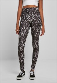 Colanți cu imprimeu leopard alb-negru, cu talie înaltă, realizați dintr-un material elastic, asortați cu adidași negri. Textură netedă.