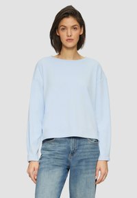 Lichtblauwe cropped sweatshirt met lange mouwen, gemaakt van zachte stof, met een brede halslijn en een relaxte pasvorm, gecombineerd met blauwe jeans.
