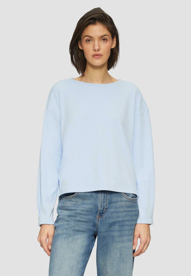 Lichtblauwe cropped sweatshirt met lange mouwen, gemaakt van zachte stof, met een brede halslijn en een relaxte pasvorm, gecombineerd met blauwe jeans.