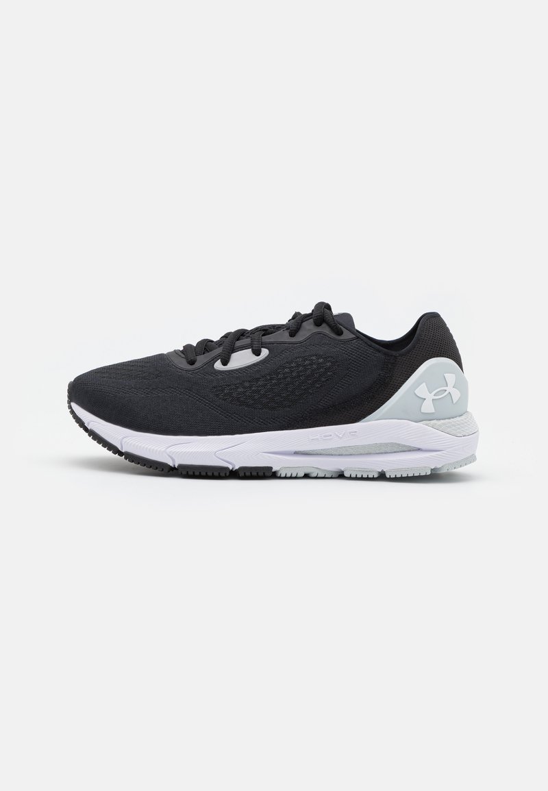 Zapatilla deportiva negra con parte superior de malla texturizada, suela blanca acolchada y acentos en gris claro. Presenta un sistema de cordones tradicional.
