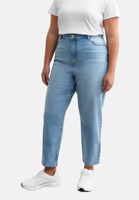Jeans de tiro alto en azul claro con corte recto, con el clásico estilo de cinco bolsillos y un sutil desvanecimiento. Combinados con una camiseta blanca y zapatillas.