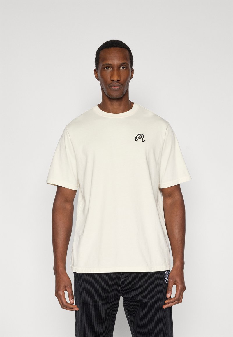 Άσπρο βαμβακερό t-shirt με κοντά μανίκια, στρογγυλή λαιμόκοψη και μαύρο κεντημένο λογότυπο στο στήθος, σε συνδυασμό με μαύρο παντελόνι από κορδόνι.