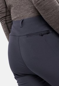 Mörkblå träningsbyxor tillverkade av elastiskt material, med en slät yta och en liten bakficka med dragkedja.