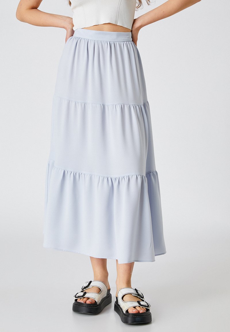 Jupe maxi bleu clair à volants en tissu doux avec une taille froncée. Portée avec des sandales noires ornées de boucles en argent.