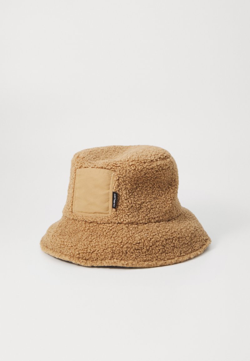 Chapeau seau en polaire marron avec une surface douce et texturée, comportant un patch en tissu beige sur le côté et un large bord flou.