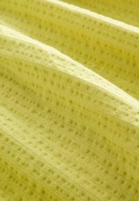 Mīksts dzeltenīgs audums ar tekstūru, kas visā virsmā ir pārklāts ar režģa rakstu. Materiāls izskatās viegls un nedaudz stiepjas.