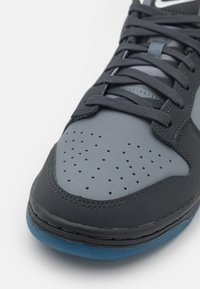 Sneaker with a gray synthetic upper, smooth texture, and perforated detail on the toe. Black laces and a blue rubber outsole.