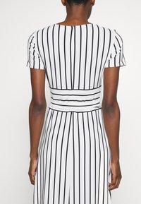 Randig klänning i svart och vitt, kort ärm, figursydd midja, slätt tyg, bakre knäppning, vertikala ränder skapar en förlängande effekt.