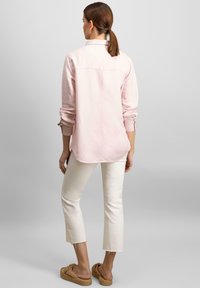 Camicia a maniche lunghe rosa chiaro con colletto e polsini arrotolati, abbinata a pantaloni cropped bianco sporco con orli sfilacciati e sandali intrecciati.