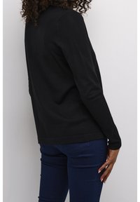 Svart långärmad topp med rund halsringning, figurnära silhuett och ribbade ärmslut. Tillsammans med mörkblå figurnära jeans.