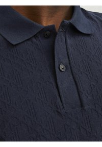 Polo de punto en color navy con un patrón texturizado, que presenta un cuello extendido y dos botones negros en el cuello.
