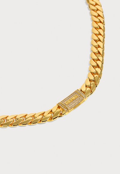 Κοντινή λήψη μιας χρυσής αλυσίδας τύπου Cuban link με ορθογώνιο κούμπωμα διακοσμημένο με μικρούς διαφανείς λίθους και χαραγμένο όνομα μάρκας.