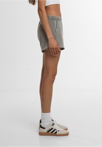 Shorts en coton gris avec une ceinture élastique, des poches latérales et une coupe décontractée, assortis de chaussettes blanches et de baskets avec des accents noirs.