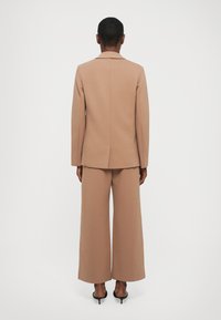 Beige sakový blazer s jedním rozparem, doplněný širokými kalhotami ve stejném odstínu. Hladká tkanina a čistý, strukturovaný silueta.