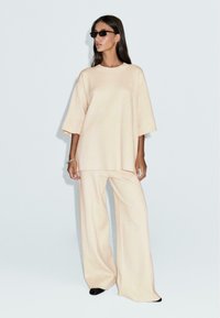 Luźny, kremowy sweter z krótkimi rękawami, zestawiony z szerokimi spodniami z tej samej tkaniny, prezentujący gładką teksturę i swobodny krój.