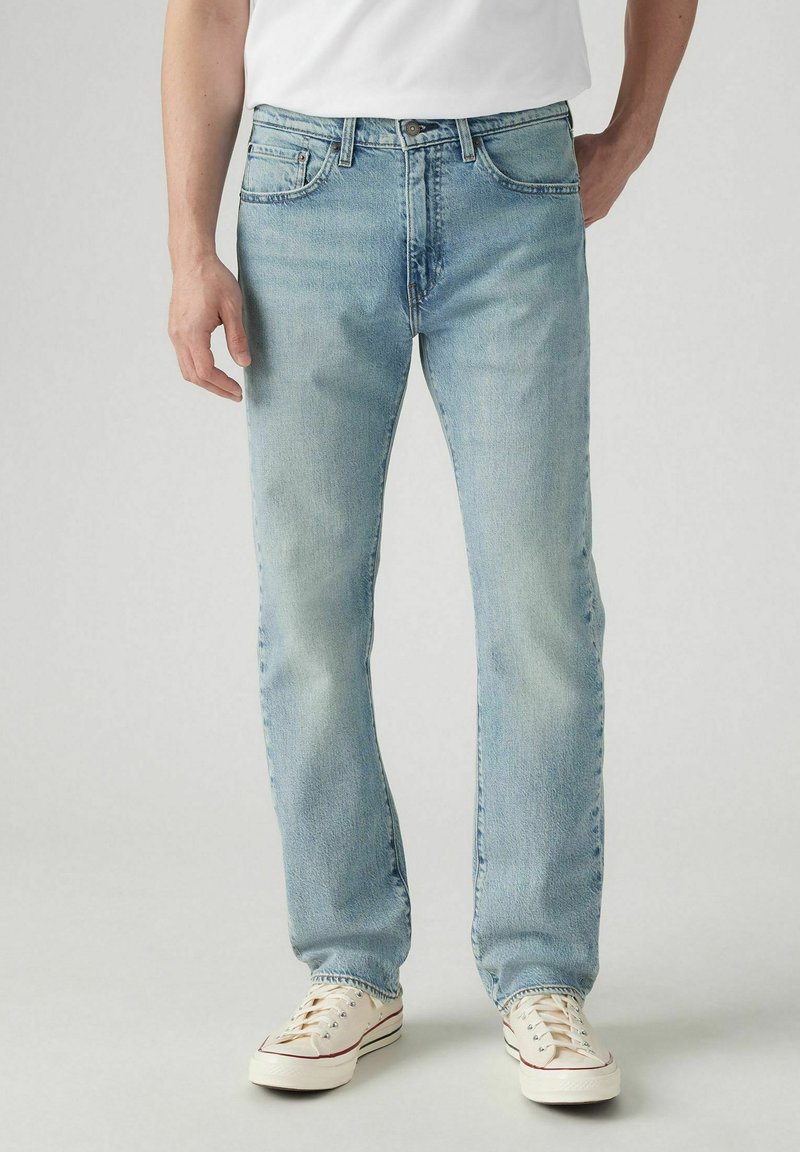 Helle blauen Denim-Jeans mit geradem Bein, fünf Taschen und klassischem Knopfverschluss. Tragen mit weißen Sneakers.