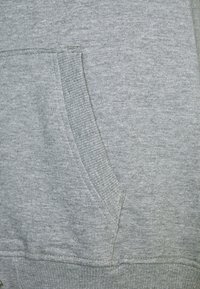 Sudadera con capucha gris claro hecha de algodón suave y texturizado. Cuenta con un bolsillo frontal, puños y dobladillo acanalados. Diseño sencillo sin patrones visibles.