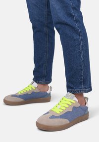 Buty sportowe z połączeniem szarego zamszu i niebieskiego dżinsu, z neonowożółtymi sznurówkami, gumową podeszwą i wiązanym wzorem.