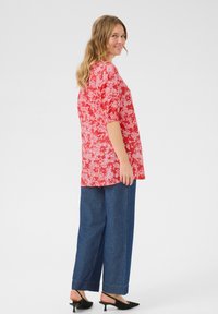 Rotes Blumenmuster-Oberteil mit Puffärmel, kombiniert mit locker sitzenden blauen Denim-Hosen und schwarzen Slippern. Einfaches, lässiges Design.