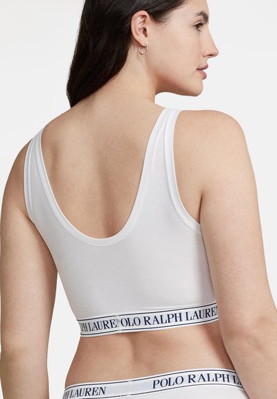 Femme vue de dos portant un soutien-gorge de sport blanc et une culotte assortie avec des bandes élastiques marquées « Polo Ralph Lauren ».
