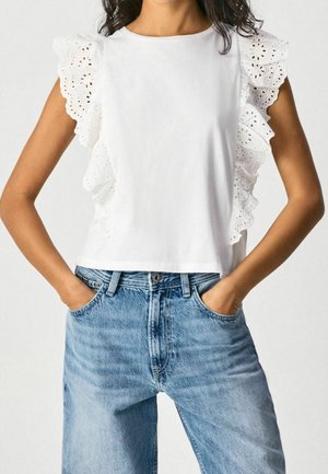 Biała bluzka z krótkim rękawem z koronkowymi falbanami, w połączeniu z jasnoniebieskimi dżinsami o wysokim stanie, które mają luźny krój i kieszenie.