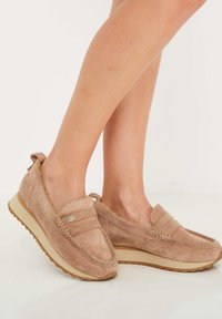 Mocasines de ante en beige claro con un acabado texturizado, que presentan un detalle de costura en la parte superior y una suela de goma para mayor agarre.