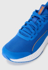 Kék hálós sportcipő kék fűzőkkel, fehér talppal és narancssárga "Puma" logóval a nyelvén.