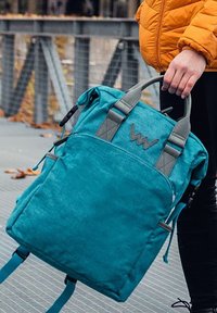 Tyrkysový batoh vyrobený z texturované látky se šedými akcenty, dvojitými rukojeťmi, nastavitelnými popruhy a logem na přední straně.