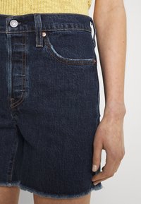 Jeansshorts i mörkblått med fransad nederkant, utrustade med koppardetaljer och framfickor. Tyget har en texturerad yta.