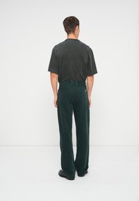 Luźne ciemnozielone spodnie z korduroyu o wysokim stanie i szerokich nogawkach, w zestawieniu z czarnym oversize'owym t-shirtem, widok z tyłu.