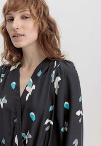 Schwarzes Wickelkleid mit floralem Muster in Türkis, Pink und Weiß. Es hat einen tiefen V-Ausschnitt und einen weichen, fließenden Stoff mit Falten an den Schultern.