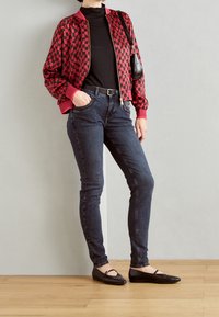 Red and black checkered bomber jacket, black top, dark skinny jeans, and black flat shoes. Smooth fabric with a fitted silhouette.