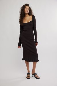 Vestido de malha castanho escuro com mangas compridas, decote quadrado e bainha evasê. A modelo usa sapatos pretos de tiras para um look contemporâneo.