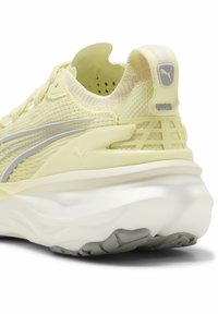 Baskets de sport jaune clair avec une tige en mesh, accents argentés, semelle intermédiaire blanche rembourrée et détails de semelle extérieure en gris texturé.