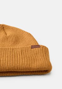 Orange knit beanie with a ribbed texture, folded cuff, and a small brown leather logo tag on the side.