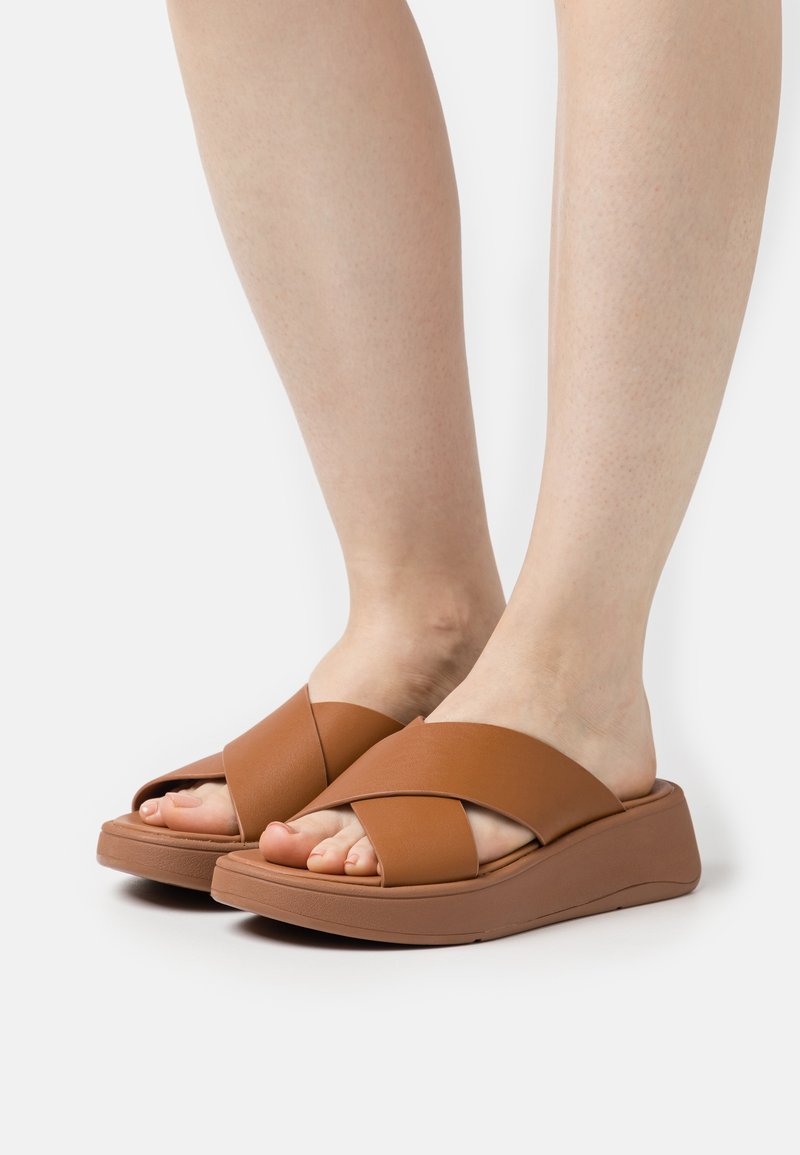 Sandali marroni con design a striscia incrociata, realizzati in materiale sintetico liscio, con una suola a cuneo imbottita per il comfort.