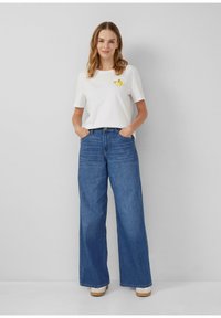 T-shirt en coton blanc à manches courtes avec un motif de citron jaune. Associé à un jean en denim bleu à jambes larges. Chaussures de couleur claire.