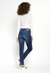 Smala jeans i mörkblå denim med en mjuk textur, med två bakfickor och minimal slitning, kombinerade med vita sneakers.