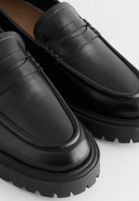 Black leather loafers with a smooth finish, featuring a raised seam and a chunky rubber sole with a tread pattern.