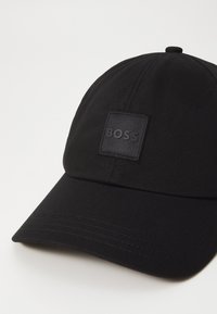 Črna bejzbol kapica iz teksturiranega blaga z kvadratnim črnim logo ploščicama z izbočenim napisom "BOSS". Ukrivljena obroba in šivani detajli.
