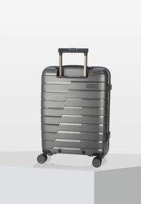 Valigia rigida nera con design a righe, manico retrattile e quattro piccole ruote per la manovrabilità. L'etichetta riporta "AIR BASE".